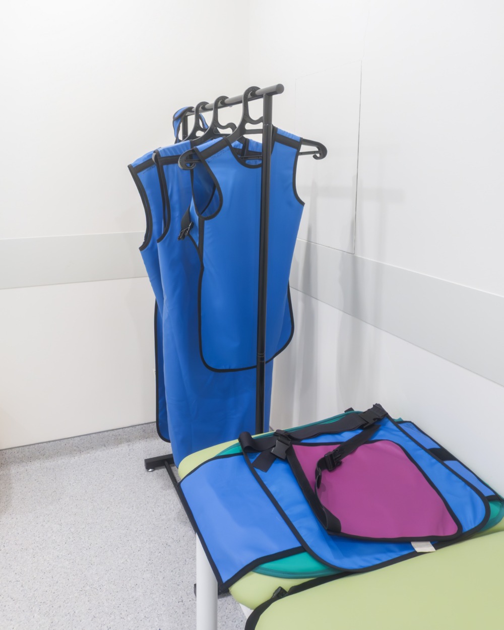 Radiation protection aprons and shielding collars wait in bright diagnostic room, ready for safe medical imaging procedures.